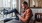 a man sits on a chair and rests his foot on a balcony railing as he looks at his phone in his room